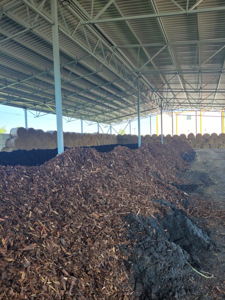 Reoveesette komposteerimisaun, kus peal näha tugiaineks kasutatavat puukoort ja taustal põhupalle (Foto: AS Emajõe Veevärk)